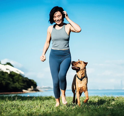 Woman walking with her dog outdoors near the lake, representing an active and healthy lifestyle